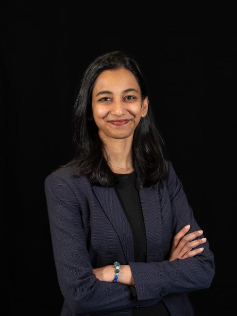 Woman in professional attire against a dark background, arms folded smiling at camera