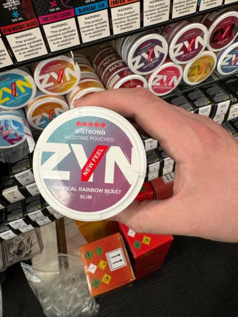 A circular package of "ZYN" branded illegal nicotine to be looking out for. With large white bolded letters noting the brand name ZYN, and mentions of a European product on the label. This product is a combination of teal and purple colored hues with white letters. This product fits in your hand. 