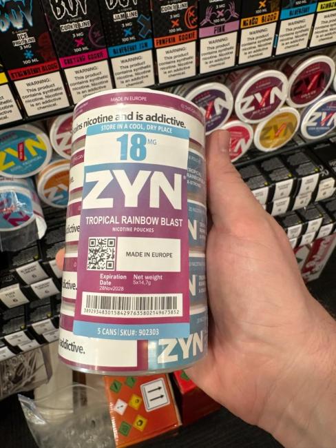 A circular package of "ZYN" branded illegal nicotine to be looking out for. With large white bolded letters noting the brand name ZYN, and mentions of a European product on the label. This product fits in your hand, is teal, with a purple label and white letters.