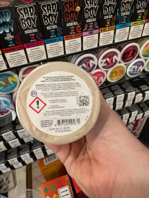 A circular package of "ZYN" branded illegal nicotine to be looking out for. With large white bolded letters noting the brand name ZYN, and mentions of a European product on the label. This product fits in your hand, the package is white, with a white label. 